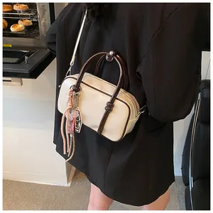 Détail du sac Boston en cuir crème, poignées marron et breloque dans un décor de vie quotidien