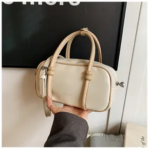 Détail du sac Boston crème avec poignées perlées et logo en relief doré élégant