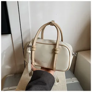 Détail du sac Boston crème avec poignées brunes et bandoulière tenu par une personne