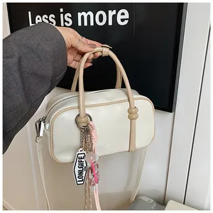 Détail du sac à main Boston avec étiquette logo et charme tissé tenu par un mannequin chic