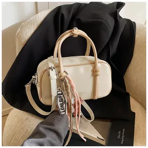 Détail du sac Boston blanc crème avec doubles poignées et breloques décoratives
