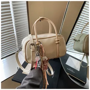 Détail d'un sac Boston cylindre beige avec pendentif peluche et bandoulière réglable