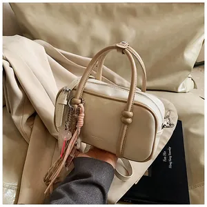 Gros plan du sac Boston crème avec poignées marron et breloques décoratives