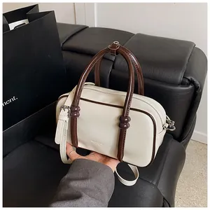 Détail du sac Boston avec poignées contrastées marron et texture cuir crème