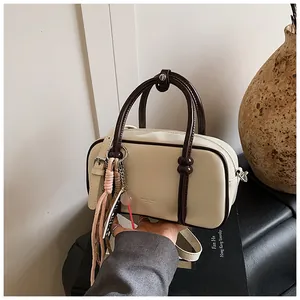 Détail du sac Boston crème avec bordure marron et pendentif pompon tissé coloré