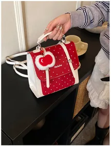 Detail der roten Handtasche mit weißen Punkten, Apfel-Plüschanhänger und Golddetails