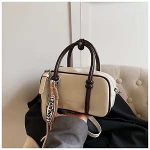 Gros plan du sac Boston crème avec poignées marron foncé et détails du logo de marque