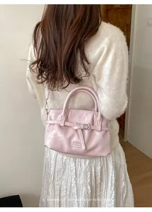 Detail view of light pink leather handbag with metal buckle worn by a model in soft light