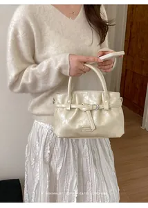 Close-up of minimalist cream white bucket bag with buckled strap and glossy finish