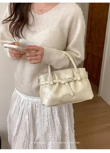 Close-up of cream retro handbag featuring knot buckle detail and a minimalist metal plate