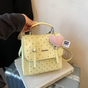 Schicker gelber Polka-Dot Rucksack mit Plüschherz vor einem stilvollen Reisekoffer