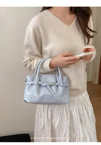 Detailed close-up of light blue leather handbag with elegant knot strap and metal logo
