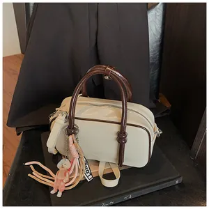 Détail du sac Boston crème avec garniture marron et charm de poupée sur des livres