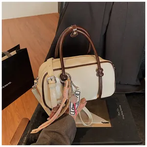 Vue détaillée du sac Boston crème avec anses marron et pompon rose sur un livre
