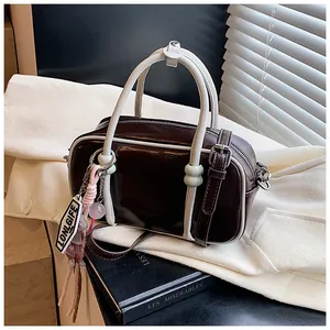 Détail du sac Boston marron foncé en similicuir avec bordures ivoire et breloque chic