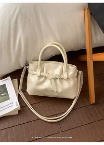 Detail of a creamy white leather bucket bag with ruched design and belt buckle accent