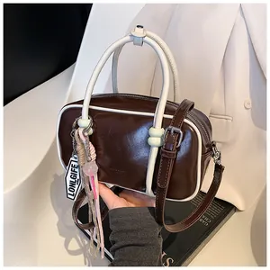 Vue détaillée d'un sac Boston rétro marron foncé avec bordure blanche et gland rose