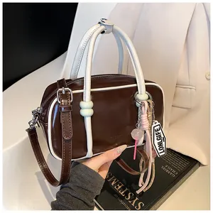 Détail du sac Boston marron foncé avec poignées contrastées blanches et breloques