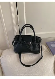 Detail of a minimalist black leather bucket bag on a sofa with retro design and strap