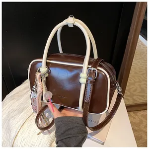 Gros plan du sac Boston marron avec surpiqûres blanches et pendentifs décoratifs