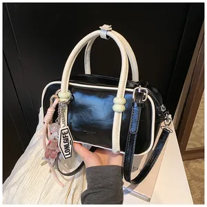 Vue détaillée du sac Boston en cuir brillant noir avec passepoils blancs et breloque logo