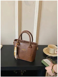 Detail einer braunen Kunstleder-Eimertasche mit Perlenanhänger und Marken-Schriftzug