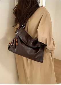 Detail of dark brown pleated tote bag with wooden bead tassel on a khaki coat