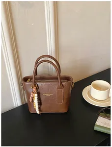 Detail der braunen Kunstleder-Eimertasche mit böhmischem Perlenanhänger und Goldaufdruck