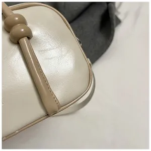 Gros plan sur la texture du cuir crème et la décoration sphérique de la bandoulière du sac