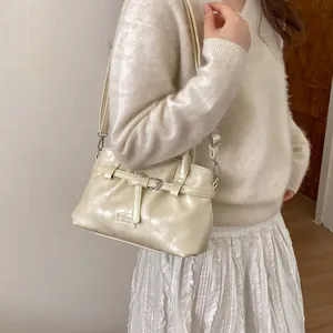 Chic beige glossy leather bucket bag with adjustable strap and retro buckle detail
