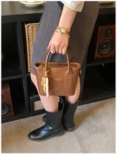 Detailansicht der braunen Ledertasche mit Perlenanhänger und Markenschriftzug