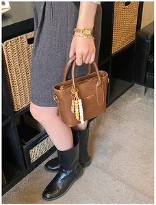Detail einer braunen Lederhandtasche mit Doppelgriffen und einem Perlen-Anhänger