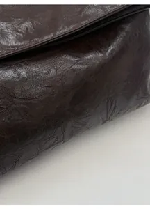 Close-up of textured brown leather tote bag with embossed silver metallic lettering