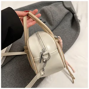 Vue détaillée du sac Boston crème avec poignées marron et pendentif à pompon tissé coloré