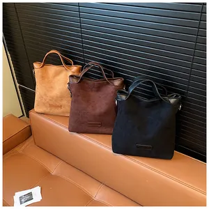 Trois sacs à bandoulière en daim marron, café et noir posés sur un canapé en cuir