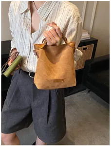 Détail d'un sac seau en daim marron avec deux poignées et un empiècement logo