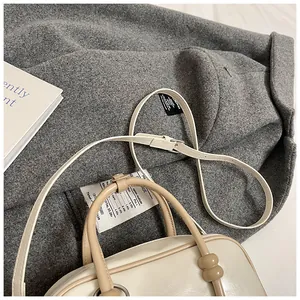Vue détaillée d'un sac Boston crème avec poignées marron sur un manteau en laine
