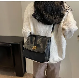 Detail of black leather tote bag with gold flower buckle on white knit sweater