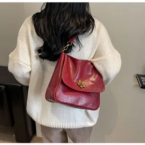 Detail of burgundy leather tote featuring a gold floral clasp on a knit sweater