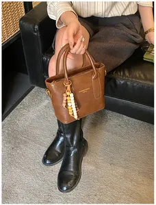 Detaillierte Nahaufnahme einer braunen Ledertasche mit Holzperlen-Anhänger und Handgriffen