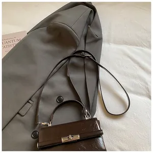 Detail of dark brown leather handbag with silver lock buckle on a grey suit jacket