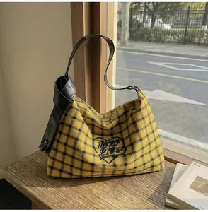 Detail of yellow and black plaid tote bag with wide knotted leather strap on window sill