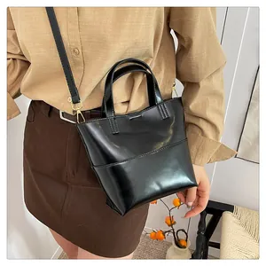 Detail of minimalist black faux leather handbag showing glossy finish and gold hardware