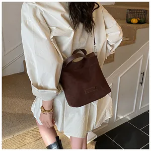 Détail du sac seau en daim marron foncé avec étiquette de marque et fine bandoulière