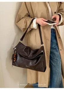 Detail of dark brown leather tote bag with wooden bead charm on a khaki trench coat