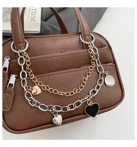 Close-up of brown lychee leather handbag with decorative metal chains and heart charms