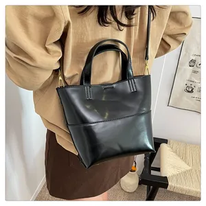 Detail of glossy black leather tote bag with sturdy handles and metallic strap connectors