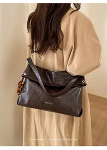 Detail of dark brown pleated leather tote bag with wooden bead charm and white lettering