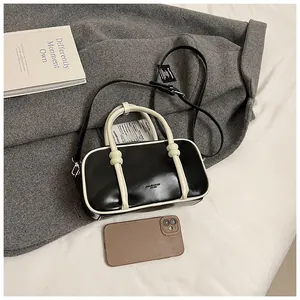 Détail du sac Boston bicolore en cuir brillant noir avec des poignées blanc crème contrastées