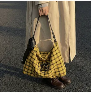 Detail of yellow plaid tote bag with black leather handle and Noro Live text design